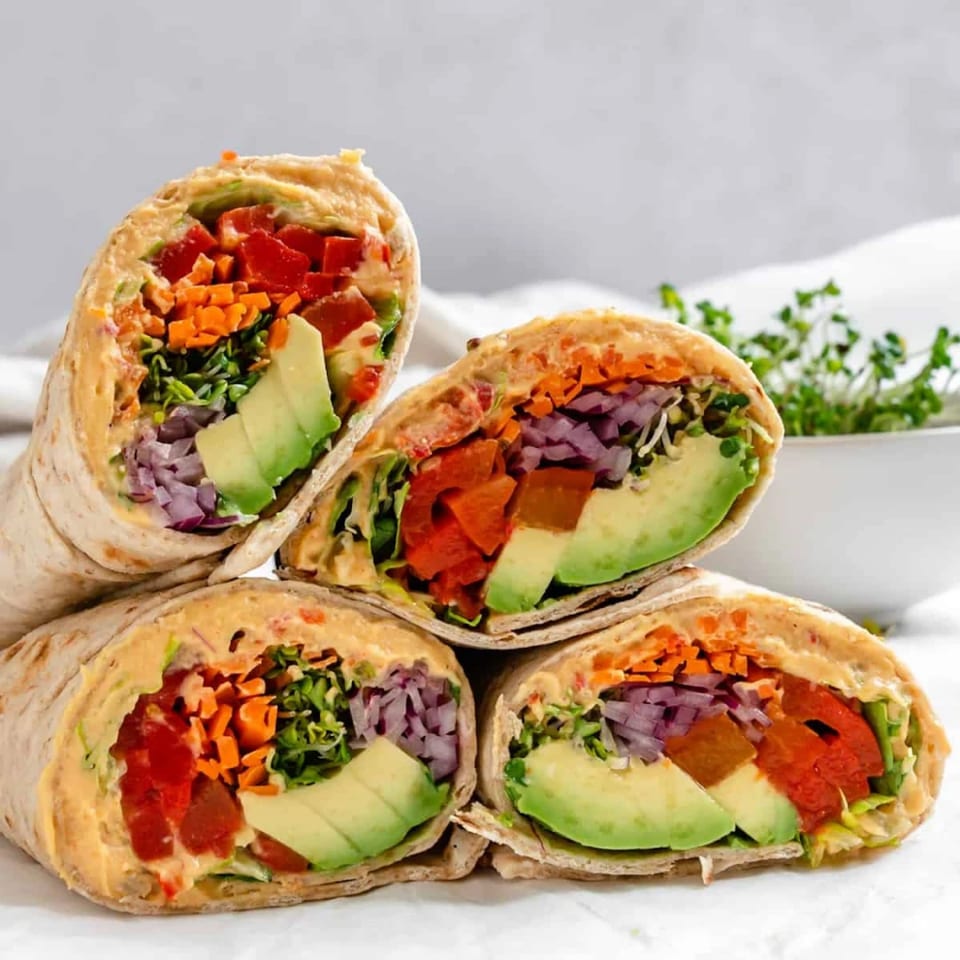 Four halal wraps, cut in half, revealing avocado, red peppers, carrots, and red onions.