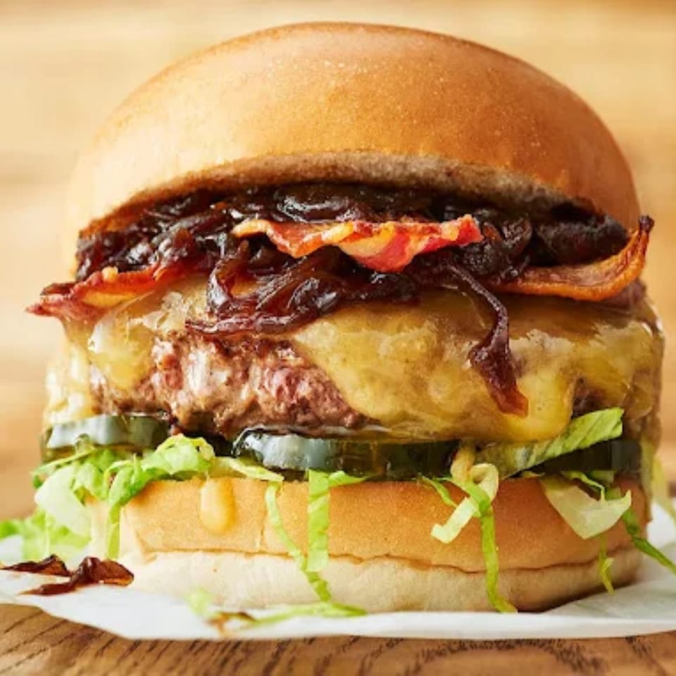 A juicy halal burger with melted cheese, caramelized onions, bacon, pickles, and lettuce on a bun.