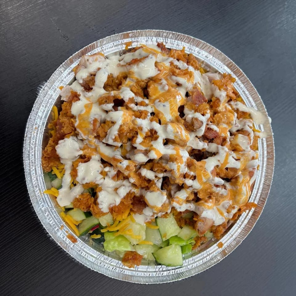 Top-down view of a halal platter with crispy chicken, white sauce, and orange sauce over salad.