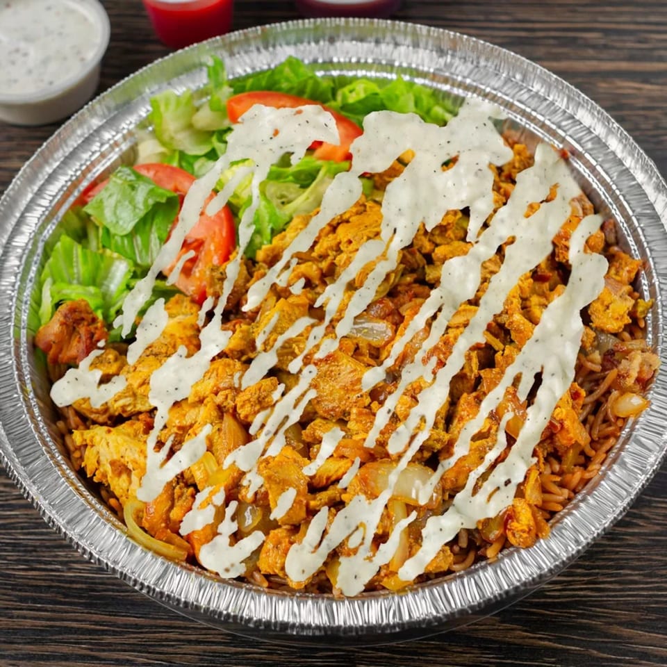 A halal platter with chicken, rice, lettuce, tomatoes, and white sauce in a foil container.