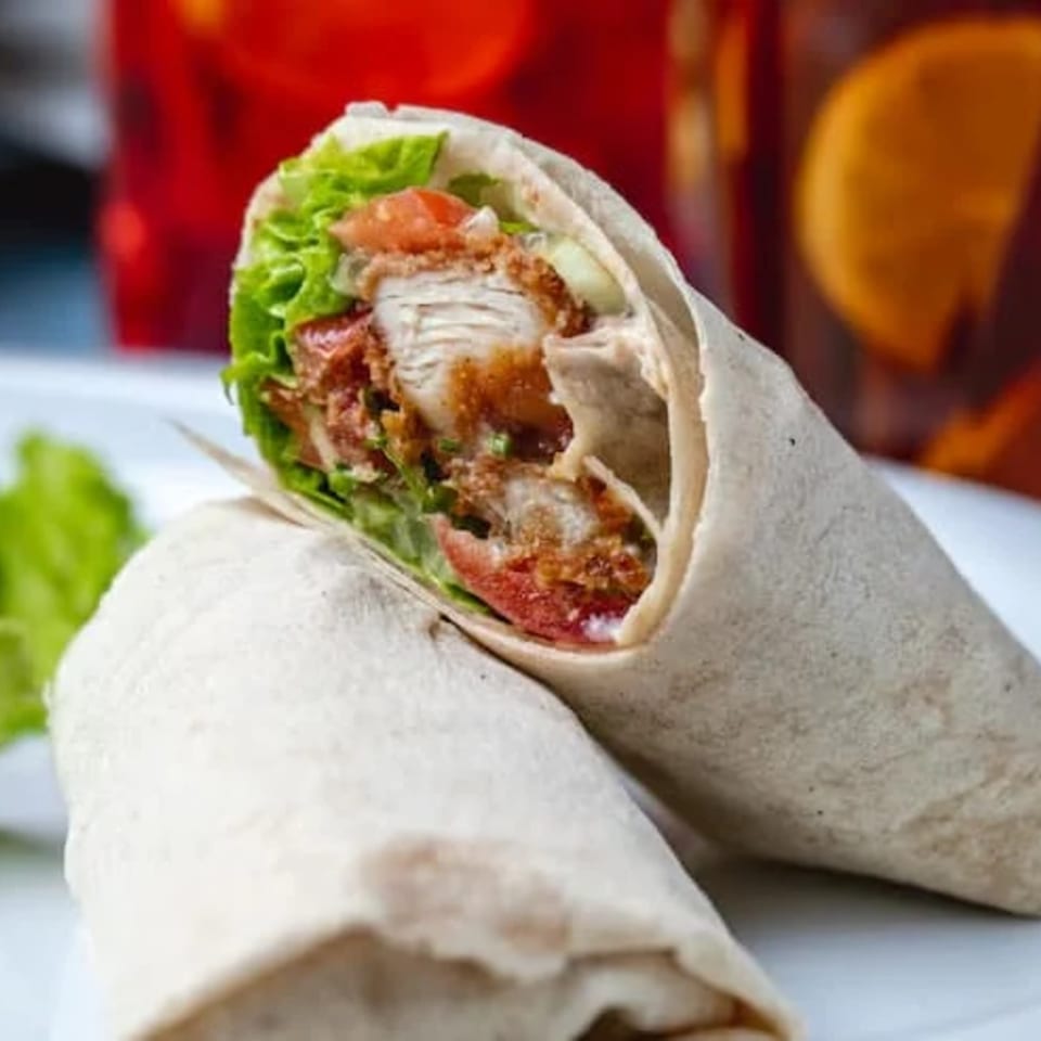 Two halal chicken wraps, filled with crispy chicken, lettuce, and tomatoes, on a white plate.